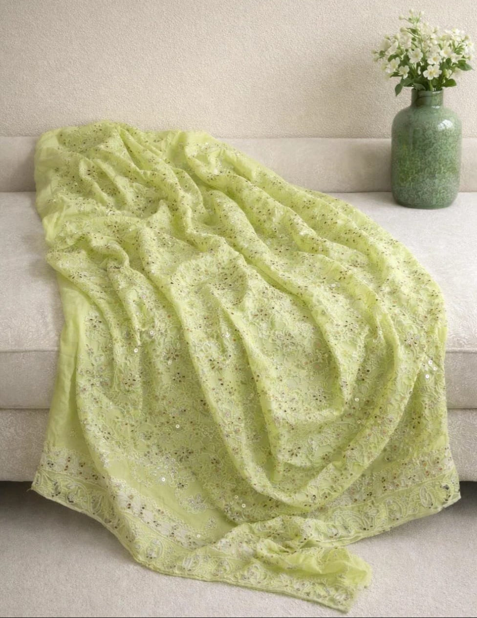 Light green blanket draped over a sofa with a vase of flowers on a matching table.
